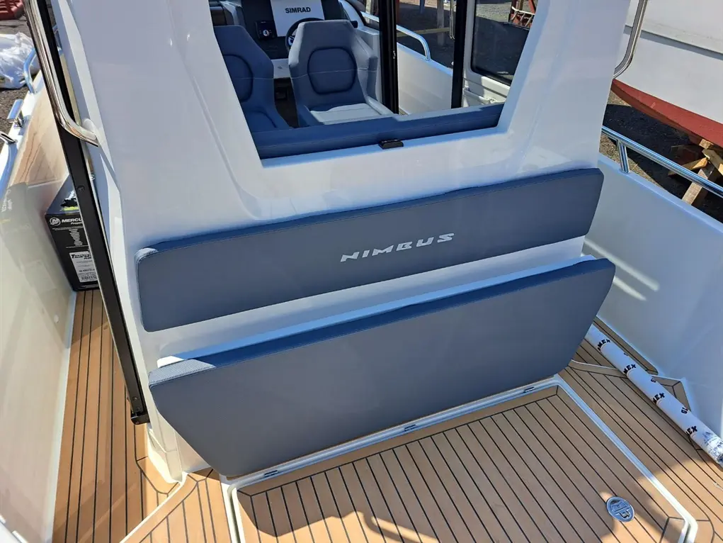 Interior view of a Nimbus boat showing blue cushioned seats, wooden flooring, and a SIMRAD dashboard.
